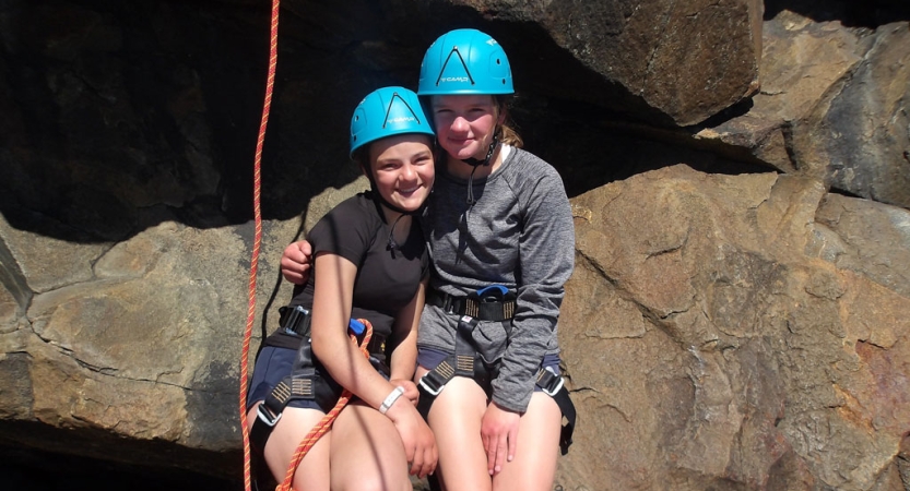 Two people wearing safety gear smile for the photo beside a large rock. 